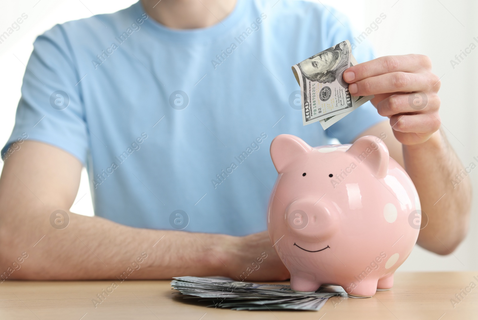 Photo of Financial savings. Man putting dollar banknote into piggy bank at wooden table, closeup