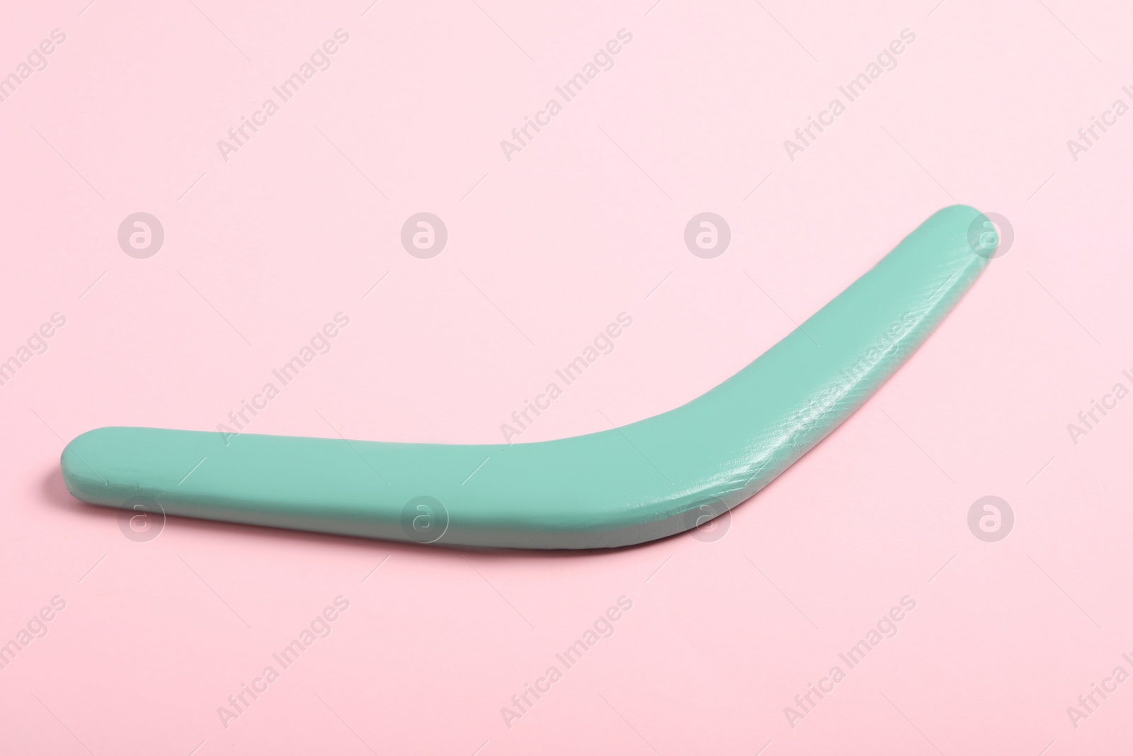 Photo of Turquoise wooden boomerang on pink background. Outdoor activity