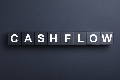 Image of Wooden cubes with phrase Cash FLow on black background, flat lay