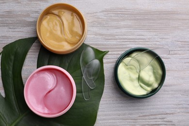Photo of Packages of different under eye patches and tropical leaf on wooden table, flat lay. Cosmetic product