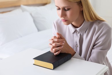 Photo of Religious young woman with Bible praying in bedroom