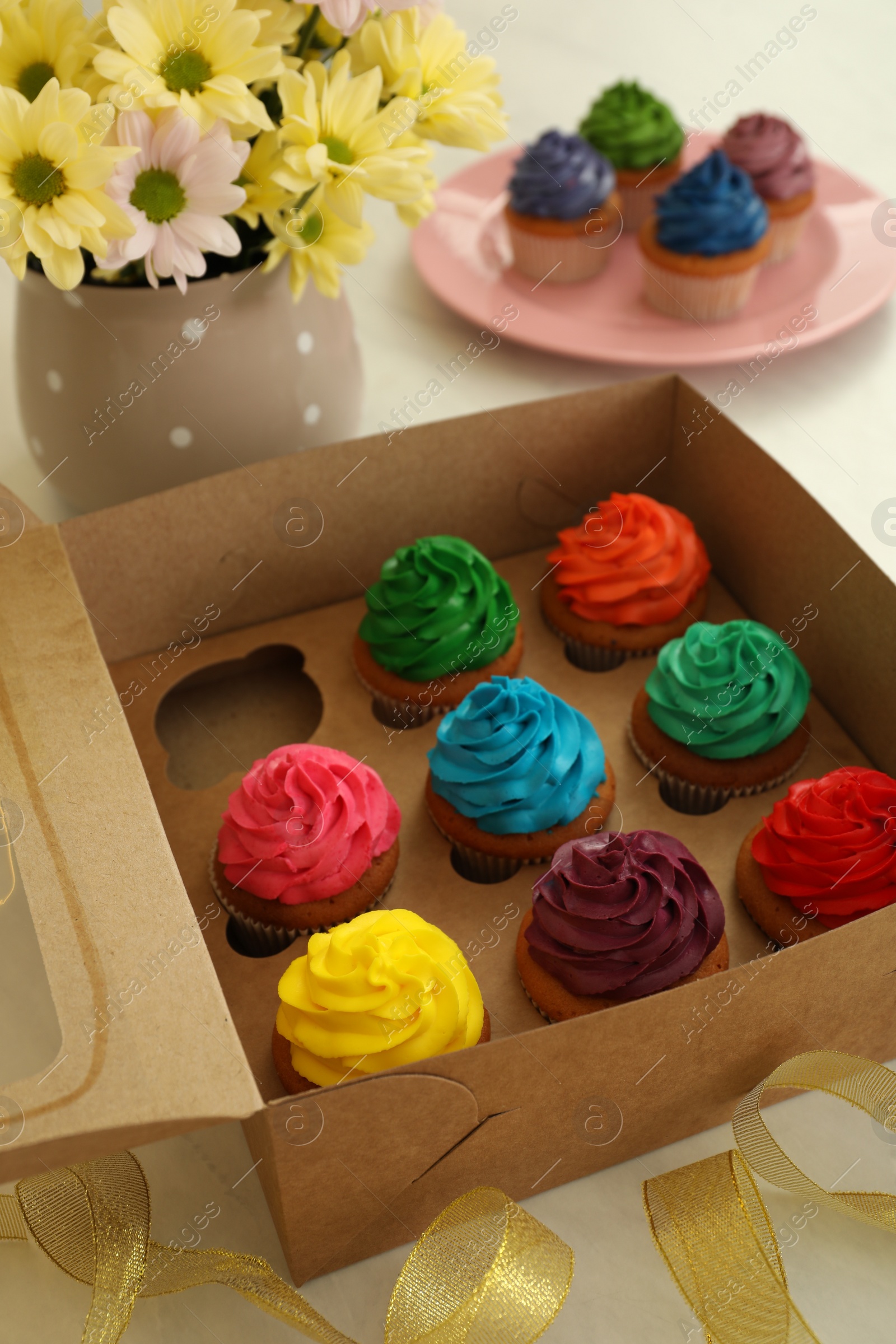 Photo of Delicious colorful cupcakes and beautiful flowers on white table