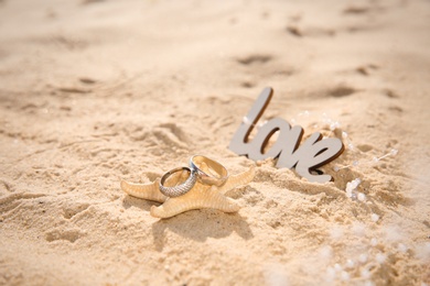 Starfish with gold wedding rings and word Love on sandy beach