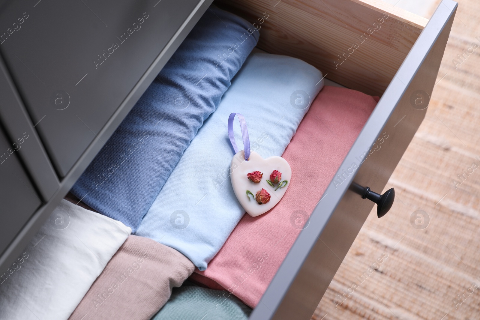 Photo of Beautiful heart shaped scented wax sachet and clothes in dresser drawer indoors, closeup