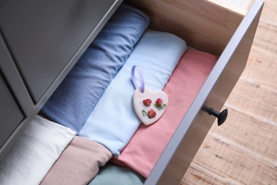 Photo of Beautiful heart shaped scented wax sachet and clothes in dresser drawer indoors, closeup