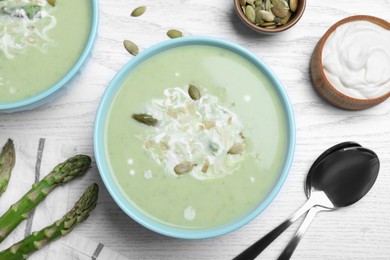 Photo of Bowls of delicious asparagus soup served on white wooden table, flat lay
