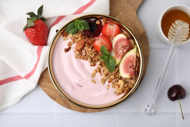 Photo of Bowl with yogurt, fruits, granola and honey on white tiled table, flat lay