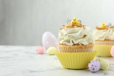 Tasty Easter cupcake with vanilla cream and candies on white marble table, space for text