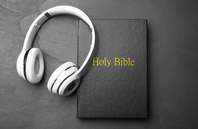 Bible and headphones on black background, top view. Religious audiobook