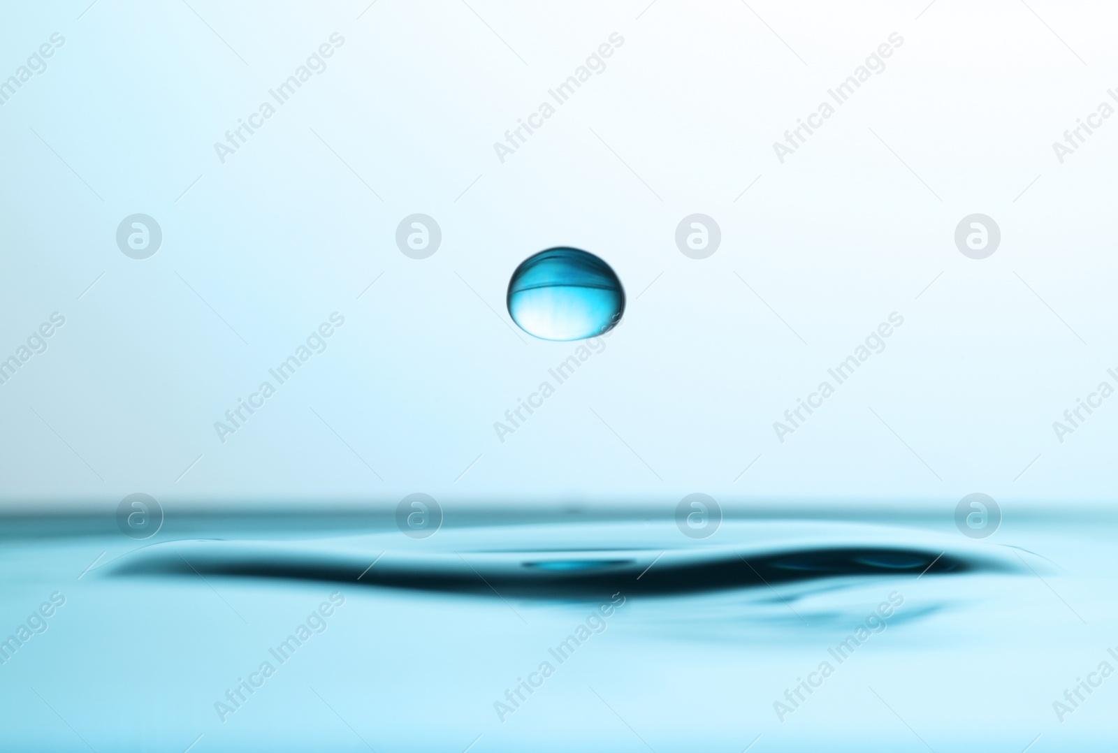 Photo of Drop falling into clear water on light background, closeup