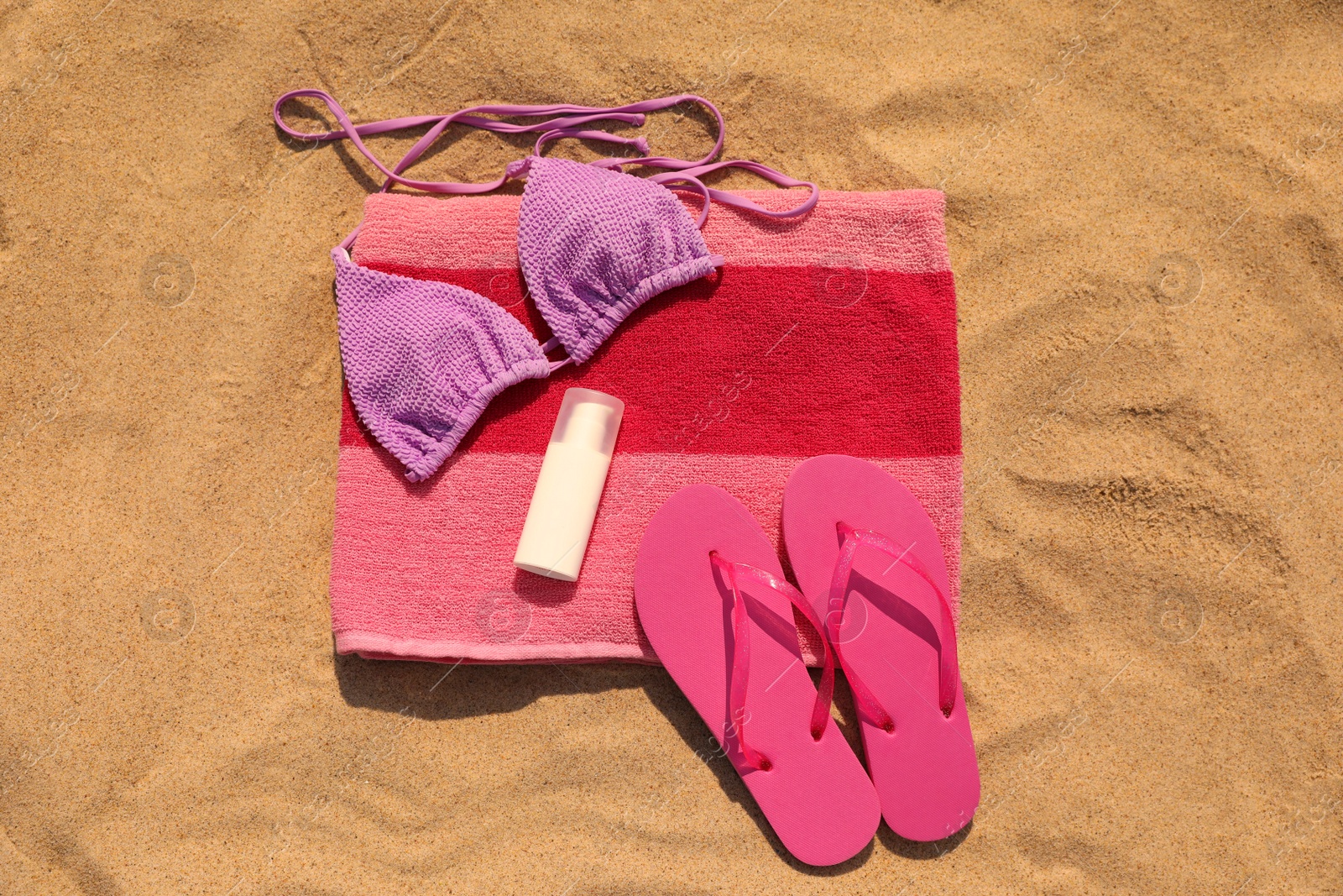 Photo of Beach towel with slippers, sunscreen and swimsuit on sand, flat lay