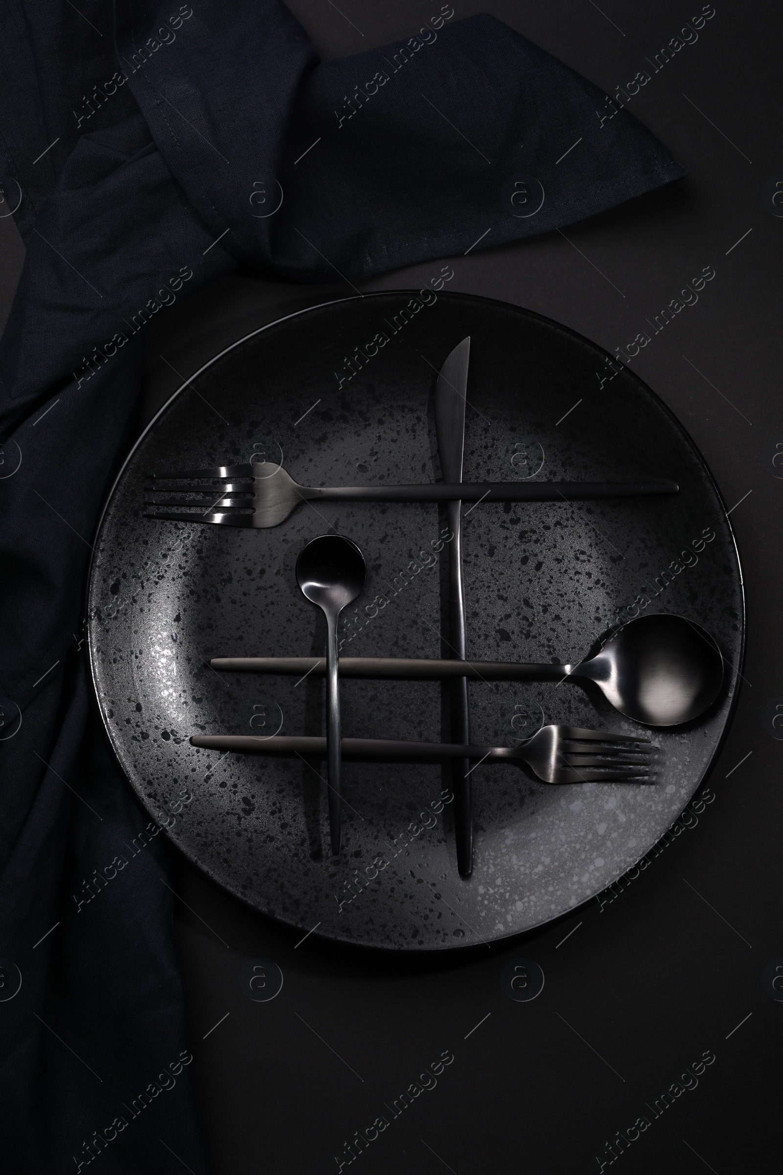 Photo of Stylish table setting. Plate, napkin and cutlery on black background, top view