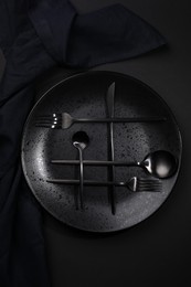 Stylish table setting. Plate, napkin and cutlery on black background, top view