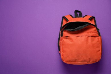 Stylish orange backpack on purple background, top view. Space for text