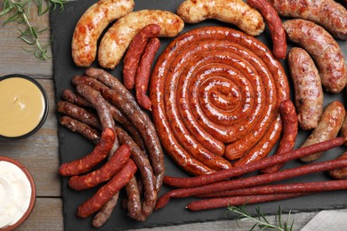 Photo of Different delicious sausages and sauces on wooden table, flat lay. Assortment of beer snacks