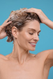 Portrait of beautiful happy woman washing hair on light blue background