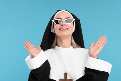 Happy woman in nun habit and sunglasses against light blue background