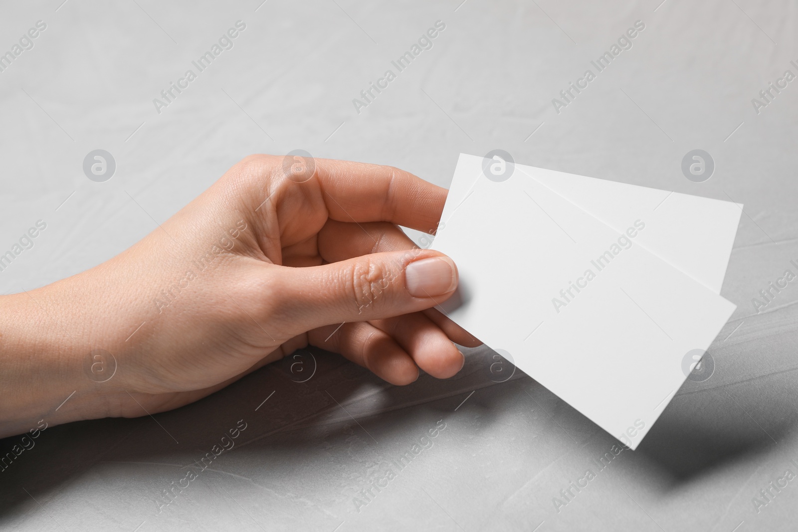 Photo of Woman holding blank cards at light grey table, closeup. Mockup for design