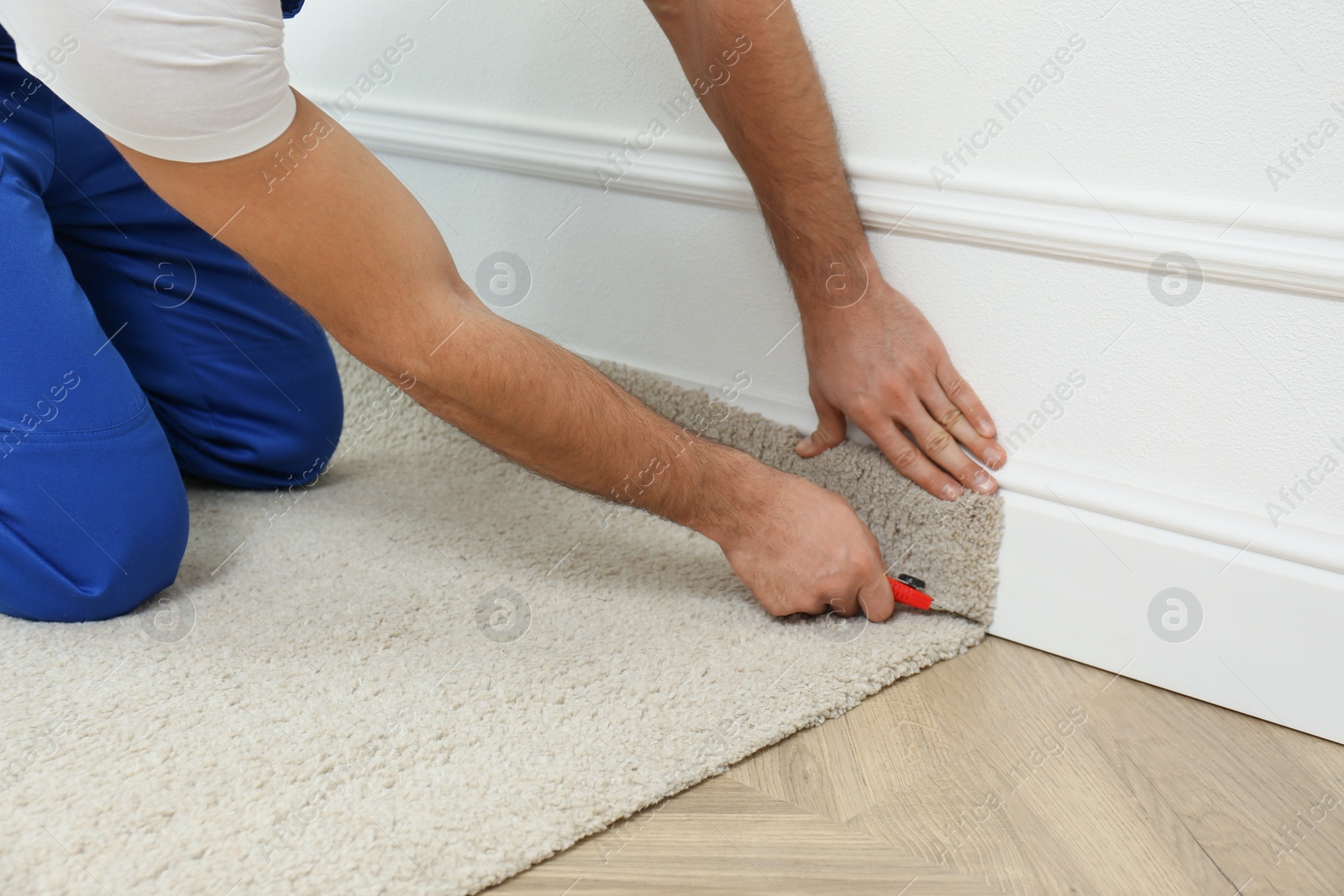 Photo of Worker with cutter knife installing new carpet indoors, closeup