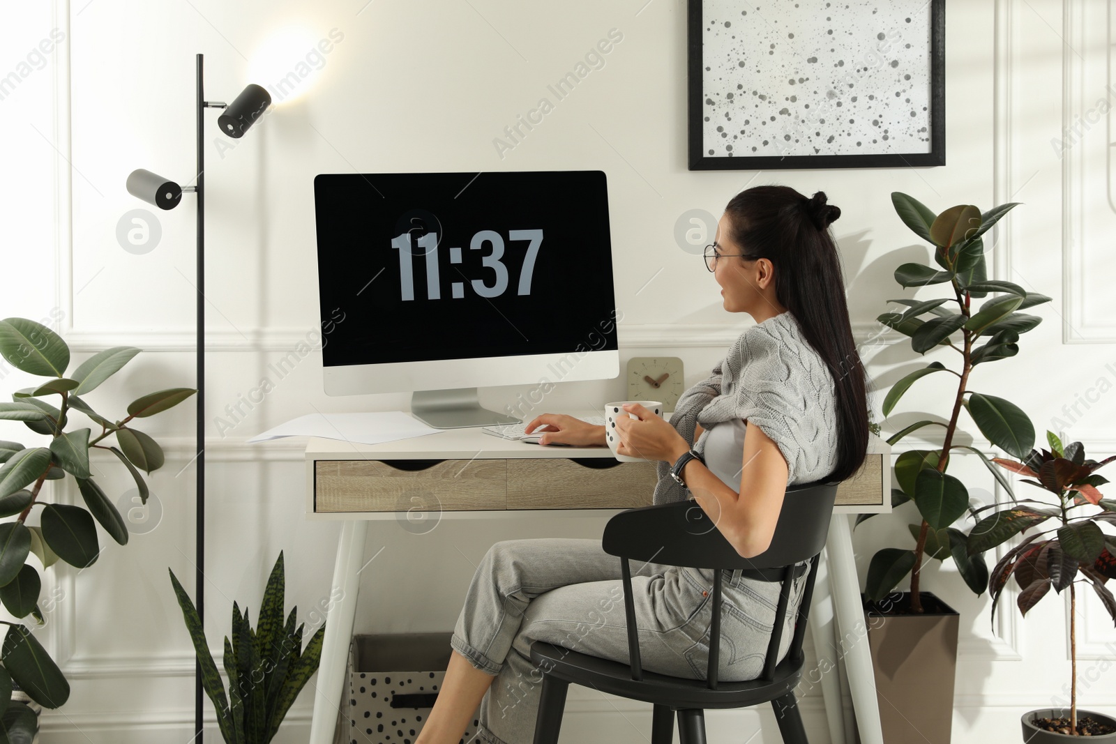 Photo of Young woman with cup of tea working at table in light room. Home office