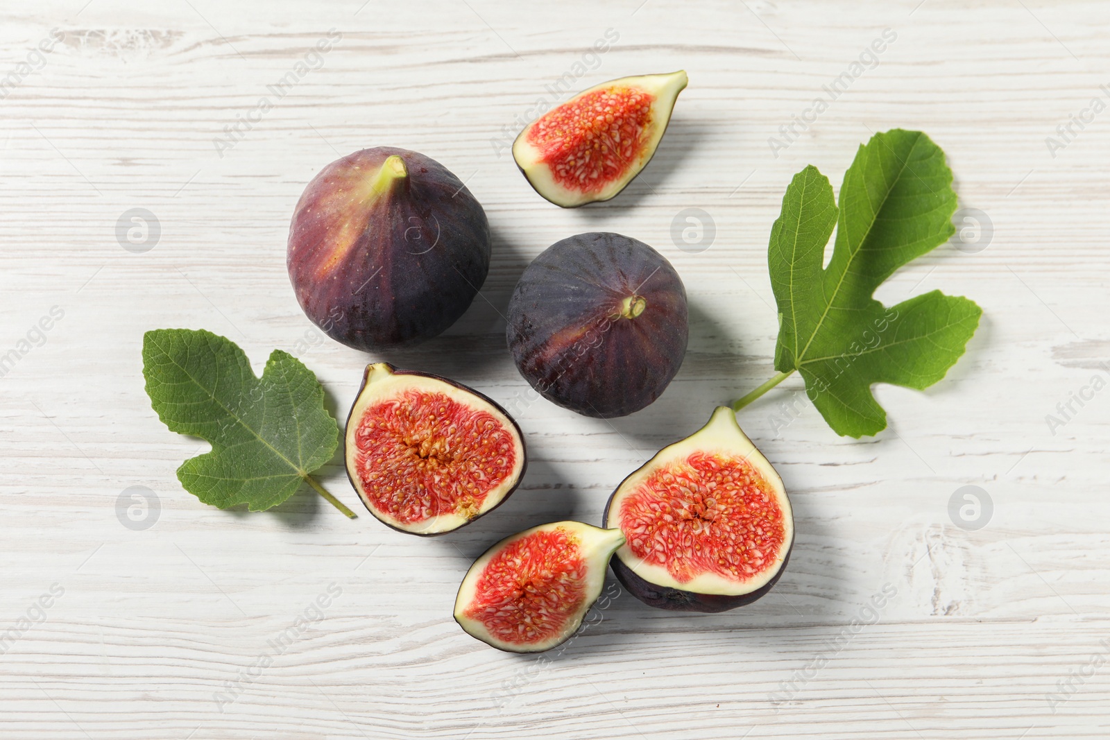 Photo of Whole and cut ripe figs with leaves on white wooden table, flat lay