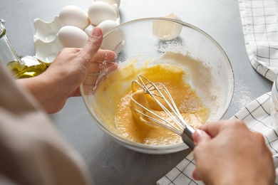 Woman whisking dough for cake at light grey table, closeup