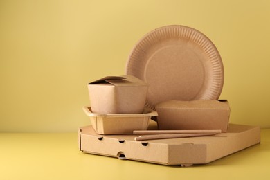 Photo of Eco friendly food packaging. Paper containers and tableware on pale yellow background, space for text