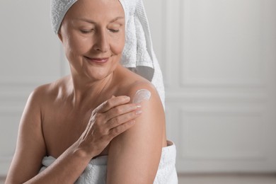 Photo of Happy woman applying body cream onto shoulder near white wall. Space for text