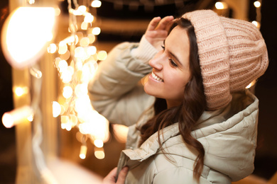 Photo of Beautiful young woman near festive lights outdoors. Winter vacation