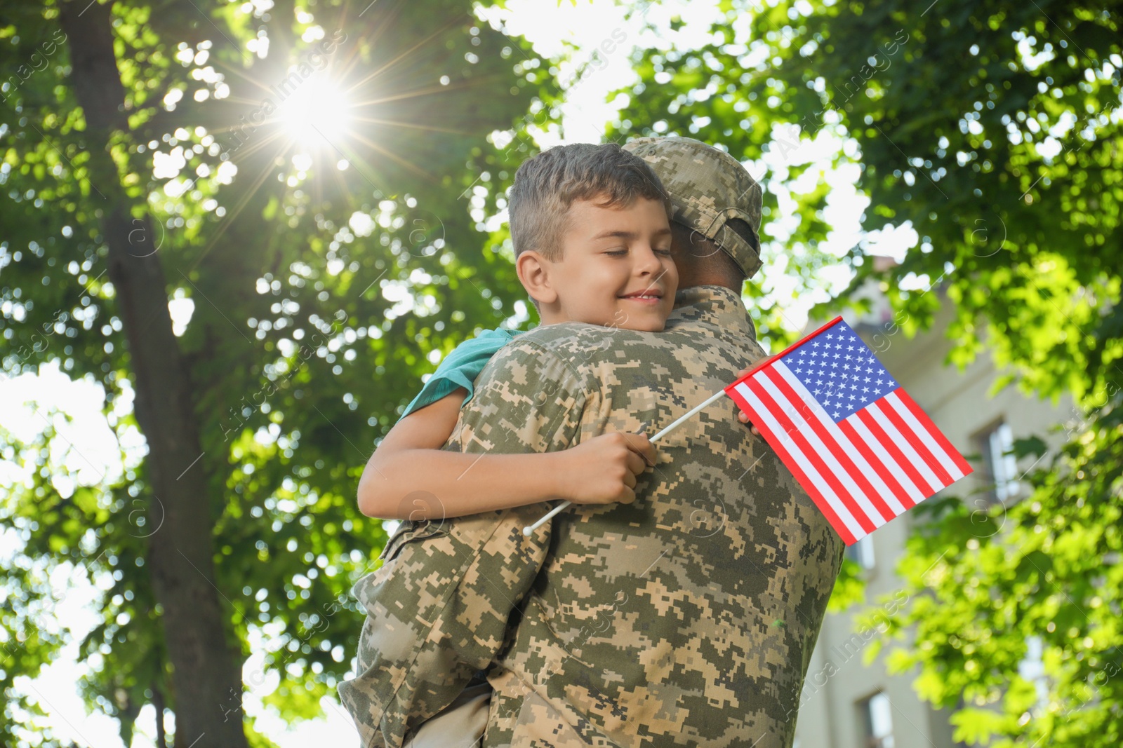 Photo of Soldier and his little son with flag of USA hugging outdoors