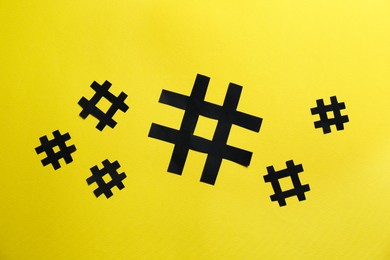Photo of Black paper hashtag symbols on yellow background, flat lay