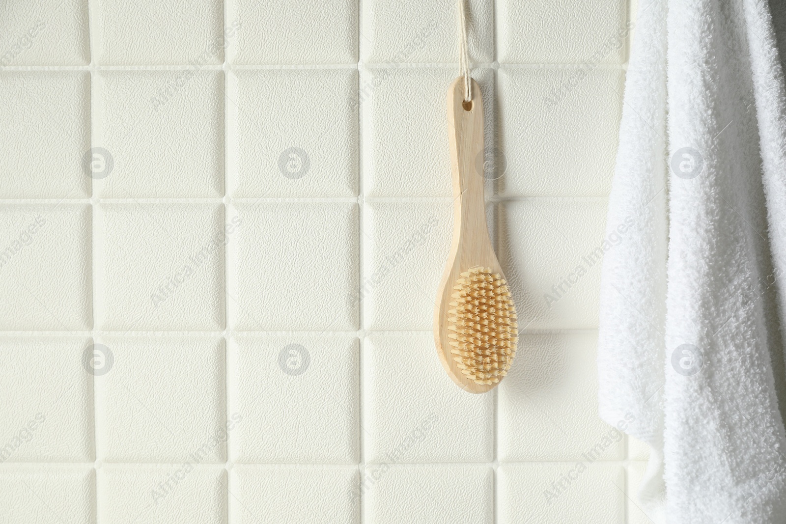 Photo of Bath accessories. Bamboo brush and terry towel on white tiled wall, space for text