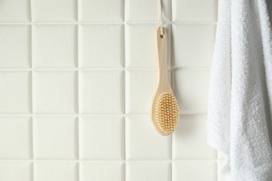 Bath accessories. Bamboo brush and terry towel on white tiled wall, space for text