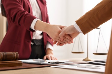 Photo of Notary shaking hands with client at table in office, closeup