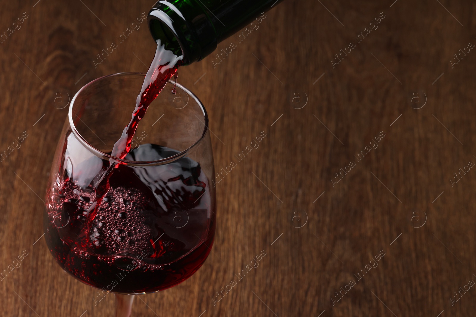 Photo of Pouring tasty red wine in glass at wooden table, closeup. Space for text