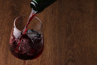 Pouring tasty red wine in glass at wooden table, closeup. Space for text