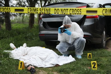 Photo of Criminologist taking photo of dead body at crime scene outdoors