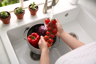 Photo of Woman washing fresh cherry tomatoes in kitchen sink, closeup