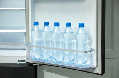 Photo of Many bottles with fresh water in fridge door bin