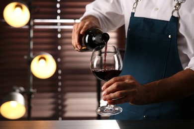 Bartender pouring red wine into glass indoors, closeup. Space for text