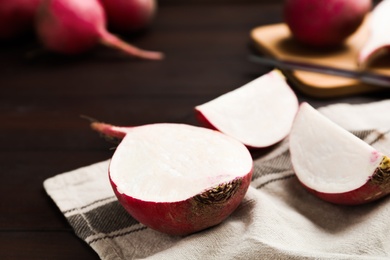 Red cut raw turnip on brown wooden table, closeup