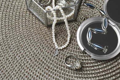 Different elegant jewelry and cosmetic pocket mirror on wicker mat. Space for text