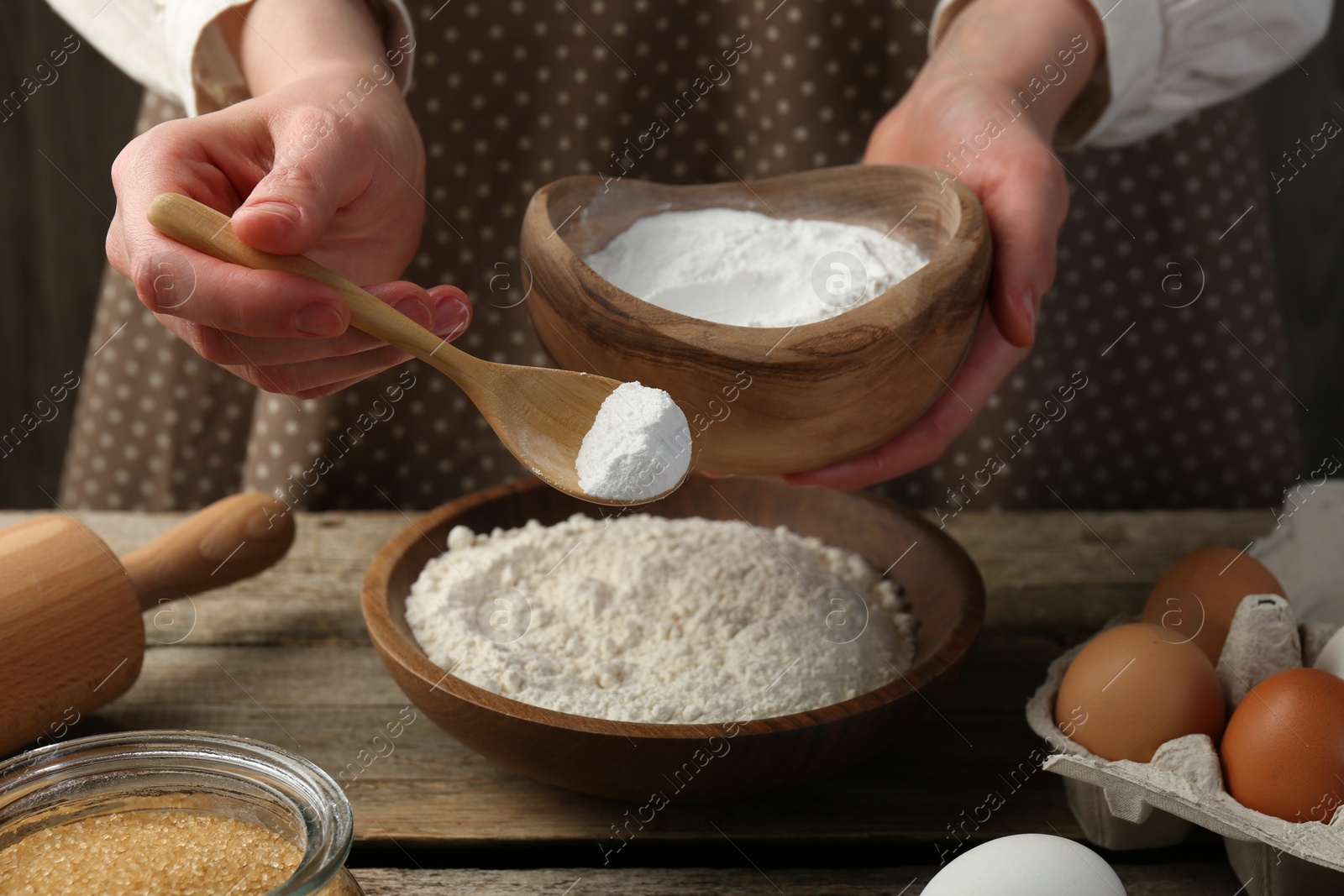 Photo of Making dough. Woman adding baking powder to flour at wooden table, closeup