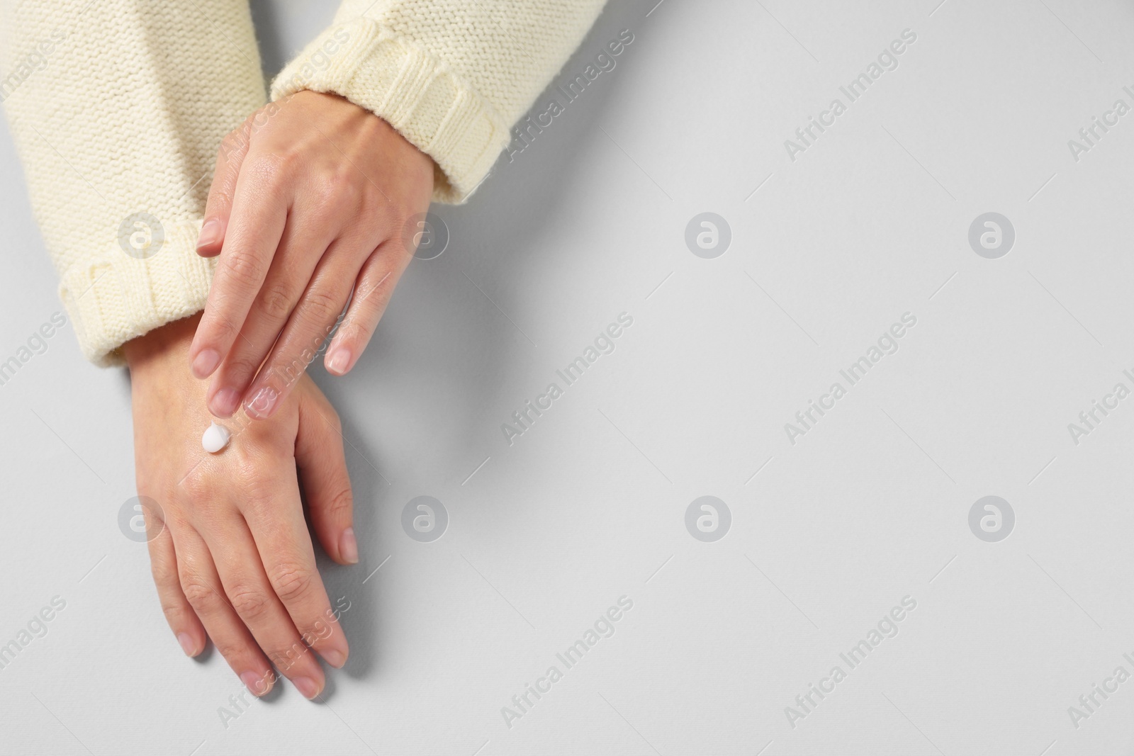 Photo of Woman applying cosmetic cream onto hand on light grey background, top view. Space for text