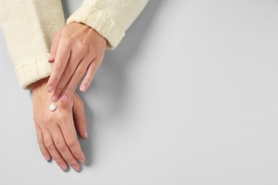 Woman applying cosmetic cream onto hand on light grey background, top view. Space for text