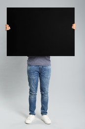 Man holding black blank poster on grey background. Mockup for design