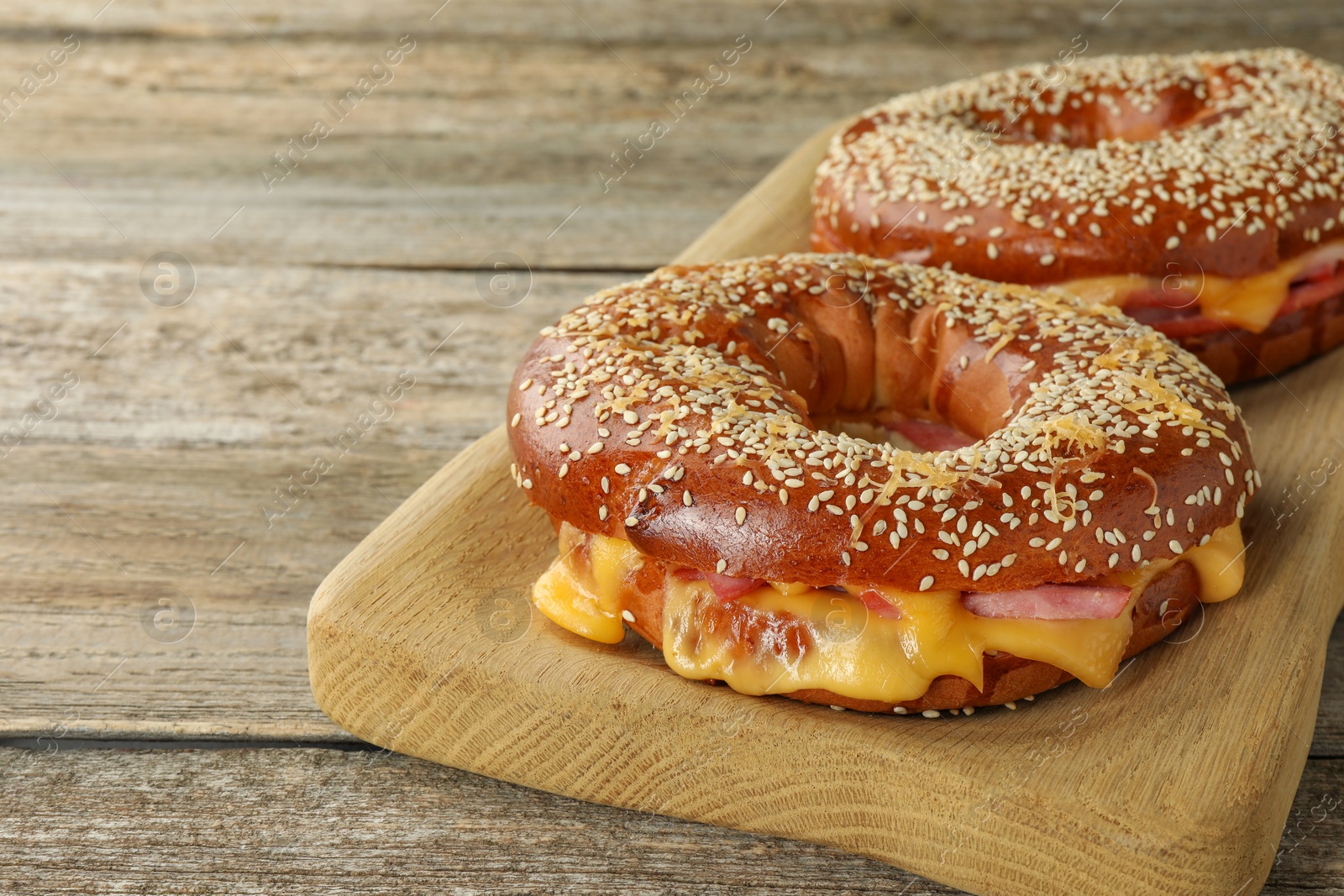 Photo of Delicious bagels with ham and cheese on wooden table, space for text