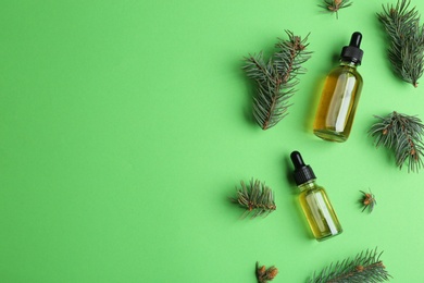 Photo of Little bottles with essential oils and pine branches on color background, flat lay. Space for text