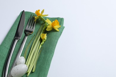 Photo of Cutlery set, Easter eggs and narcissuses on white background, space for text. Festive table setting