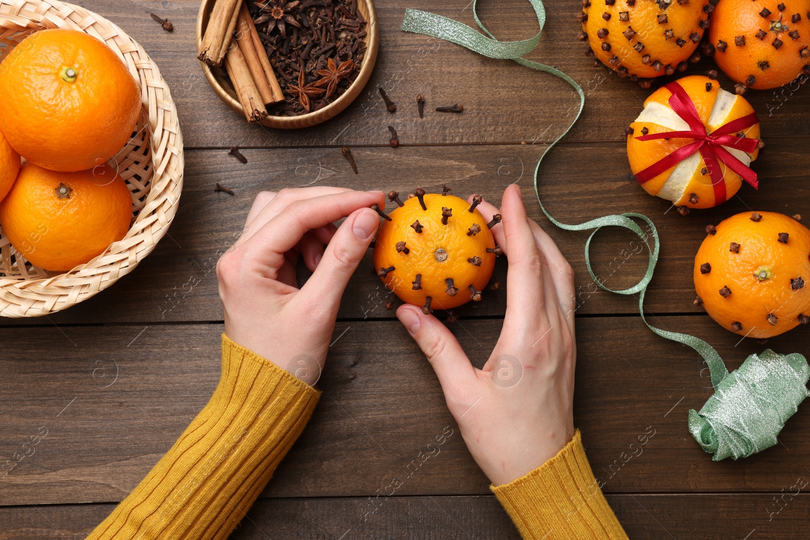 Photo of Woman decorating fresh tangerine with cloves at wooden table, top view